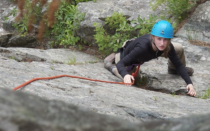 a person looks up at the camera while rock climbing on an outward bound gap year course